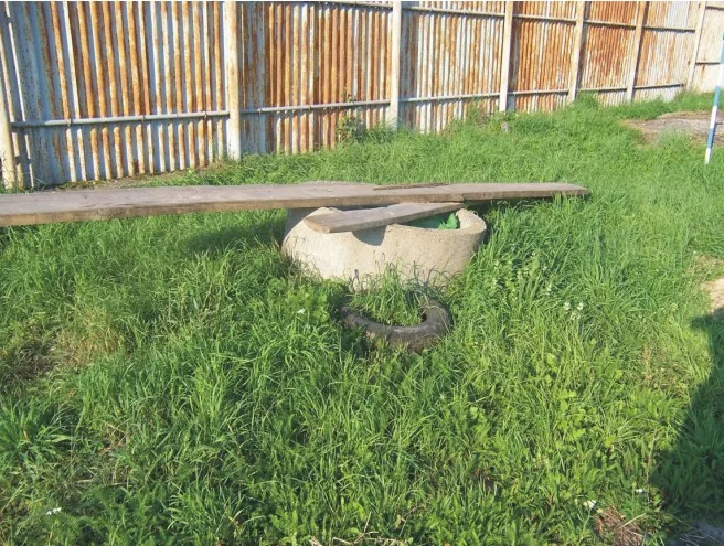 Betonový prstenec a pneumatika v trávě u plotu